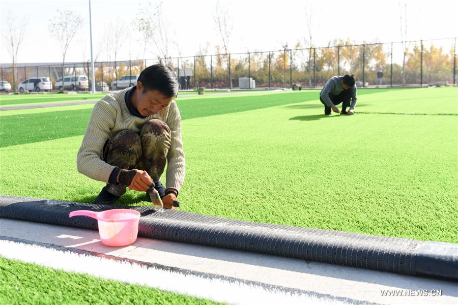 Workers pave artificial grass at a construction site of an ecological project in Changji City, northwest China