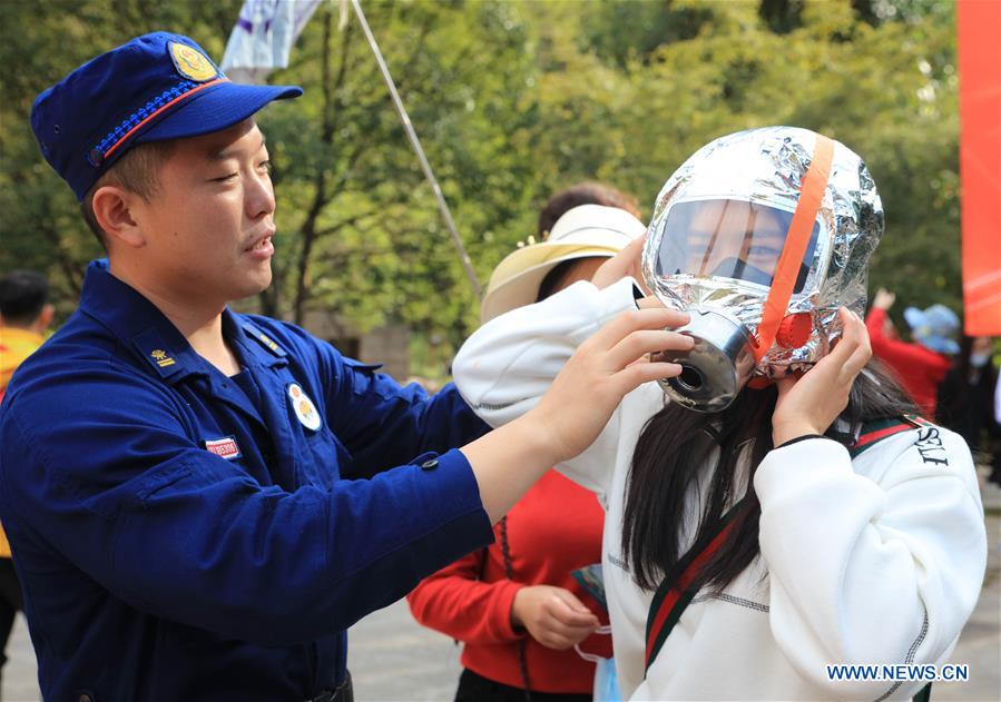 A firefighter helps as a tourist tries fire-fighting equipment at Zhangjiajie National Forest Park, central China