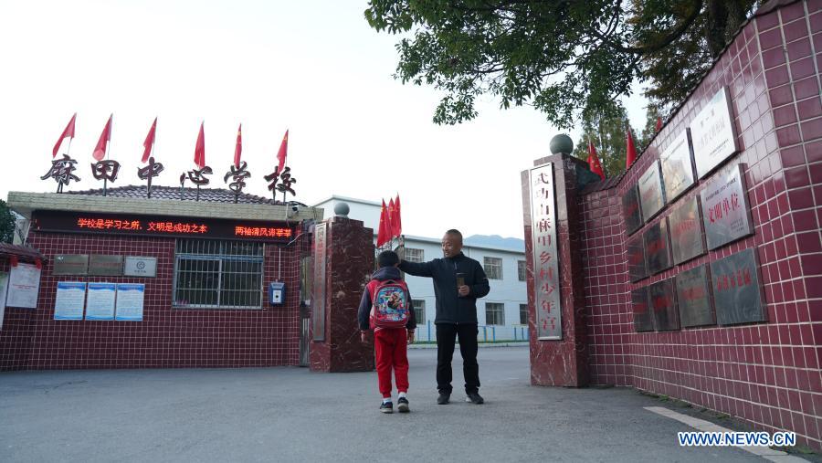Photo taken on Nov. 10, 2020 shows Zhu Zhihui (R) greeting a student at the gate of Matian School in Pingxiang, east China