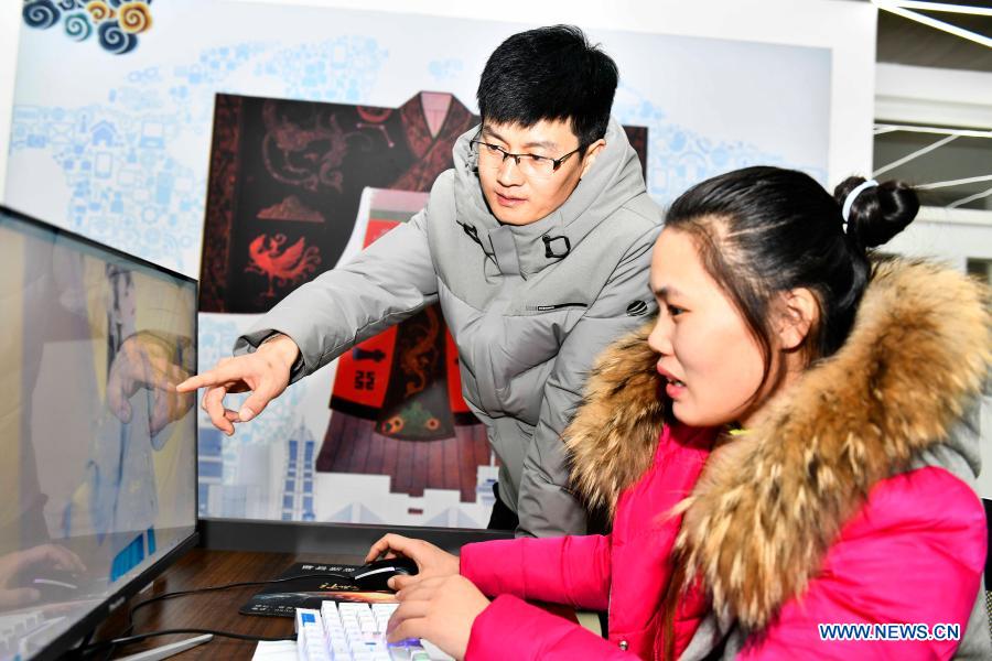 Hu Chunqing (L) communicates with a staff member about drawing designs at a secondary vocational school in Caoxian County, east China