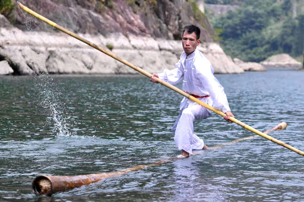 A wood surfer uses just one or two pieces of thin log and a bamboo pole to keep their balance. [Photo provided to chinadaily.com.cn]