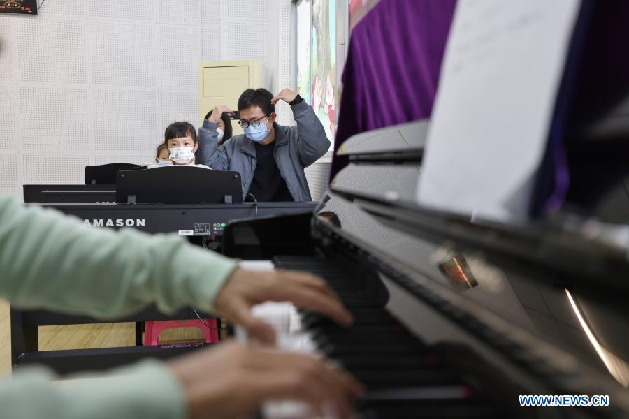 A child accompanied by her parent takes part in a free piano lesson at the youth activity center in Haikou, south China