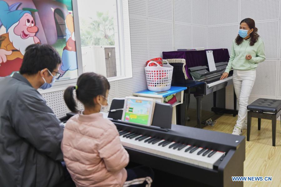 A child accompanied by her parent takes part in a free piano lesson at the youth activity center in Haikou, south China